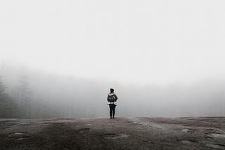 A backpacker stands in front of a forest shrouded in fog