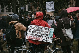 Man on bike at a Black Lives Matter rally in the rain. his sign quotes James Baldwin, nothing can be changed until it’s faced….