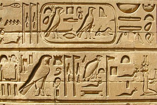 An area of a stone carving of ancient Egyptian hieroglyphs chiselled with great care and precision. The symbols shown are presented in two rows separated by a line. Some symbols are within a rounded-off box as if for emphasis.