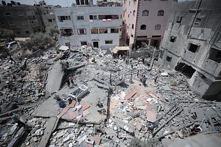 One a sunny day, with blue skies. People stand on the broken and crush rubble of their apartment building that was crushed by Israeli rocket missiles in Gaza