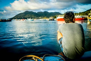 Man in blue shorts sitting by the lake and mountains