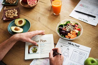 Someone planning a diet plan with foods items on the table.