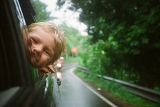 A young boy pokes his head out of a car window.