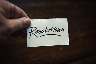 A hand holding handwritten note that reads, “Resolutions”.