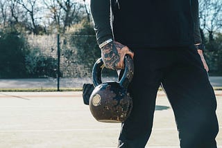 Man holding a kettlebell during an outdoor workout for strength training and fat loss.