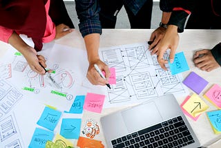 People drawing sketches on paper with post-it notes scattered on a table