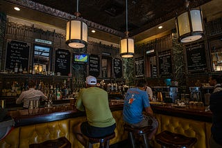 Two man sitting at a bar facing away from each other. Photo by mana5280 on Unsplash