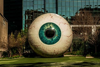 Giant sculpture of a veiny eyeball with a blue iris, on a laws outside a windowy office building