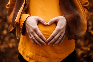 A woman holding her stomach with her hands shaped like a heart.