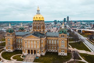 Aerial view of the gold dome of the Iowa State Capitol building with the skyline of Des Moines, Iowa, in the background.