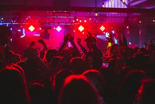 Young people with hands raised in a crowded disco. Red background.