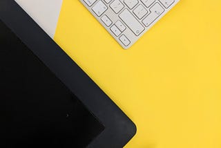 A white keyboard, a device (possibly a desktop or tablet), and a pen rests on a surface.