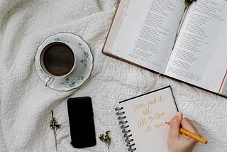 A coffee mug, phone, journal, and Bible sit on a white blanket.