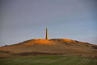 A stone monolith on top of a green hill.
