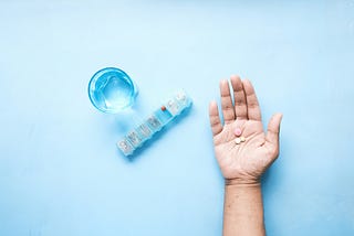 top view of pills on palm of hand with pill box and glass on water on table 