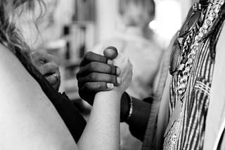 Hands of a white woman and a black man holding in mutual support.