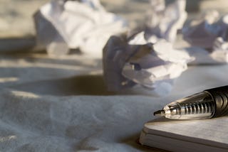 Pen sits on a notebook among crumpled papers