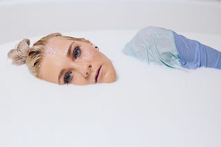 A woman’s face and shoulder showing in a milky bath