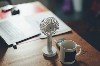 A desk with some papers, a mug, and a small fan