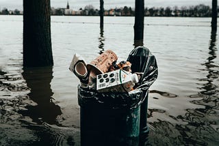 An overflowing garbage can surrounded by water in a flooded landscape