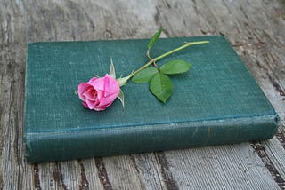 Green, hardback book with a pink rose lying on top