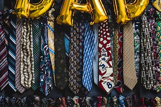 A closet filled with various dress ties. Golden Balloon letters spell out “DAD”
