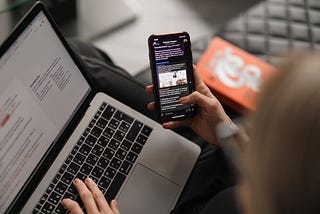 A woman with a pc on her knee, holding a smartphone