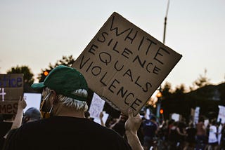 black lives matter protest, with a man holding a sign that says "white silence equals violence"
