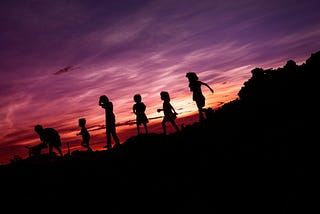 shadow of children playing on a feild with the sunset behind them