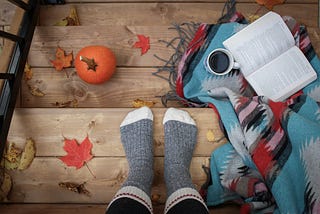 Photo of feet on a wooden steps, with an open book beside them, and a cup of black coffee.