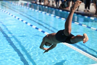 A guy diving into a competitive swimming pool during a swim race. In conjunction with my article about coaching a Men’s Division III College swim team.