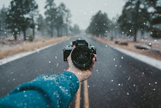 a hand holding a camera in a snowy day with mist
