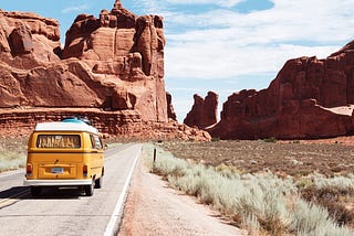 Uma kombi amarela em uma rodovia cruzando um deserto.