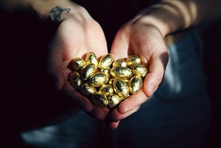 Two cupped handfuls of gold-wrapped chocolate eggs as if holding golden eggs.