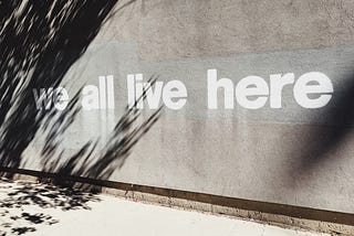 gray wall with a text graffiti saying we all live here.