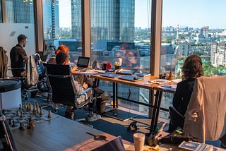 Four people working on their laptops at a long desk that is facing a window.