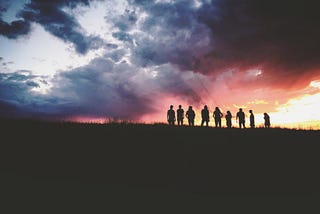 A group of people on a hill in silhouette, standing under a dramatic sunset.