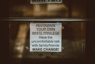 A sign taped to a wall that reads “Recognize your own white privilege. Have the uncomfortable talk with family/friends. Make change!”