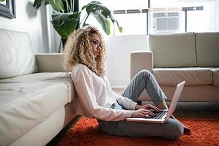Young woman sitting on the floor in her living room typing on a laptop