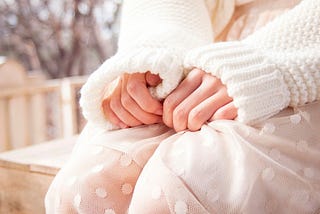 Woman in white sweater sitting with hands curled in uncertainty
