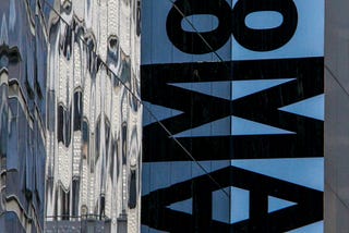 The exterior of The MOMA Museum. A sign running down the side of the building that says “MOMA”.