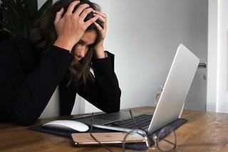 A woman sitting at a desk in front of a laptop with her head in her hands.