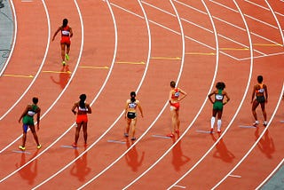 Seven women on running track starting line and one running.