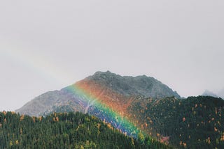 A rainbow shining over rolling hills dotted with pine trees