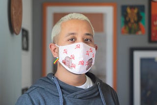 A portrait of a Britney Spears fan looking at the camera, wearing a mask with two images of Britney Spears printed on the fabric.