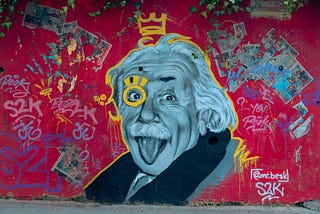 Graffiti of Albert Einstein sticking his tongue out,  painted on a red wall.