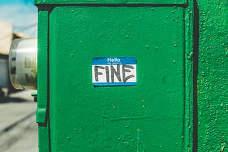 Image of green electric meter outside of building with a name tag sticker “Hello my name is” with the word “FINE” in black sharpie.