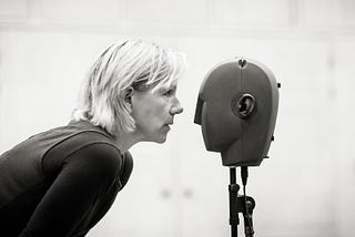 Juliet Stevenson standing face to face with a binaural microphone shaped like a human head
