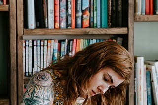 A lady writing with a book shelf behind her
