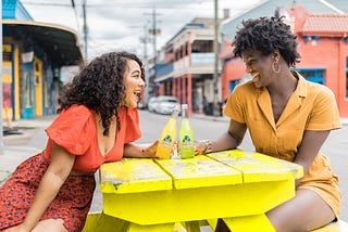 image of two women laughing while sitting at a table with drinks